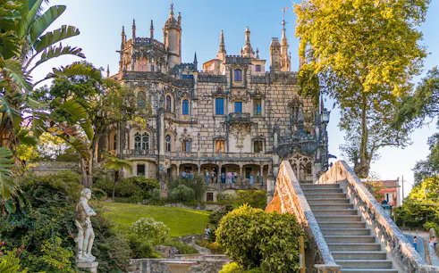 Quinta da Regaleira exterior with ornate architecture, garden, and stone staircase in Sintra, Portugal.