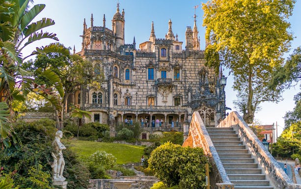 Quinta da Regaleira exterior with ornate architecture, garden, and stone staircase in Sintra, Portugal.