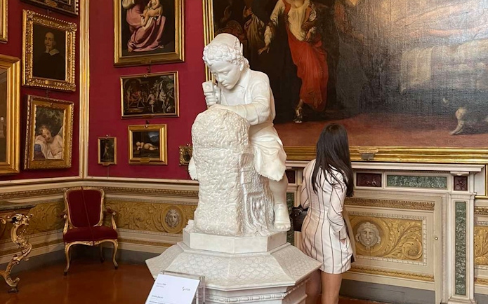 Sculpture of a child in Pitti Palace exhibition room with paintings.