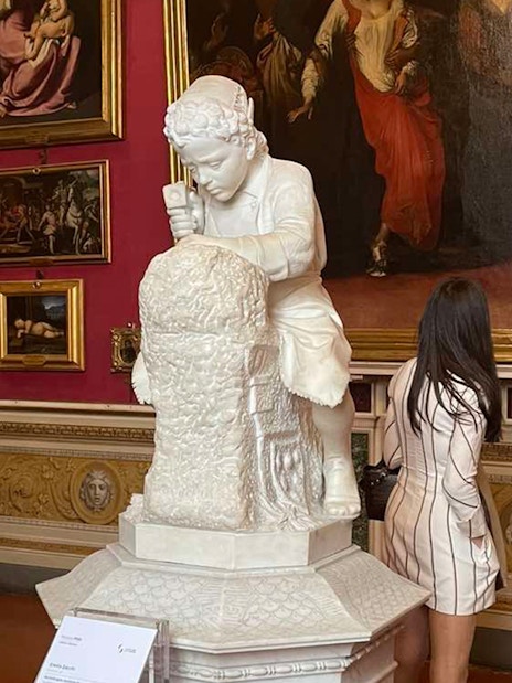 Sculpture of a child in Pitti Palace exhibition room with paintings.