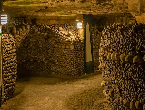 Paris Catacombs tunnel with walls of arranged skulls and bones.