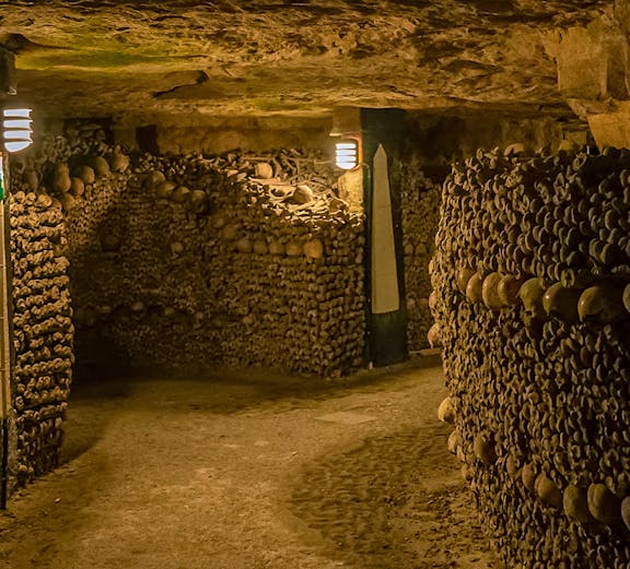 Paris Catacombs tunnel with walls of arranged skulls and bones.