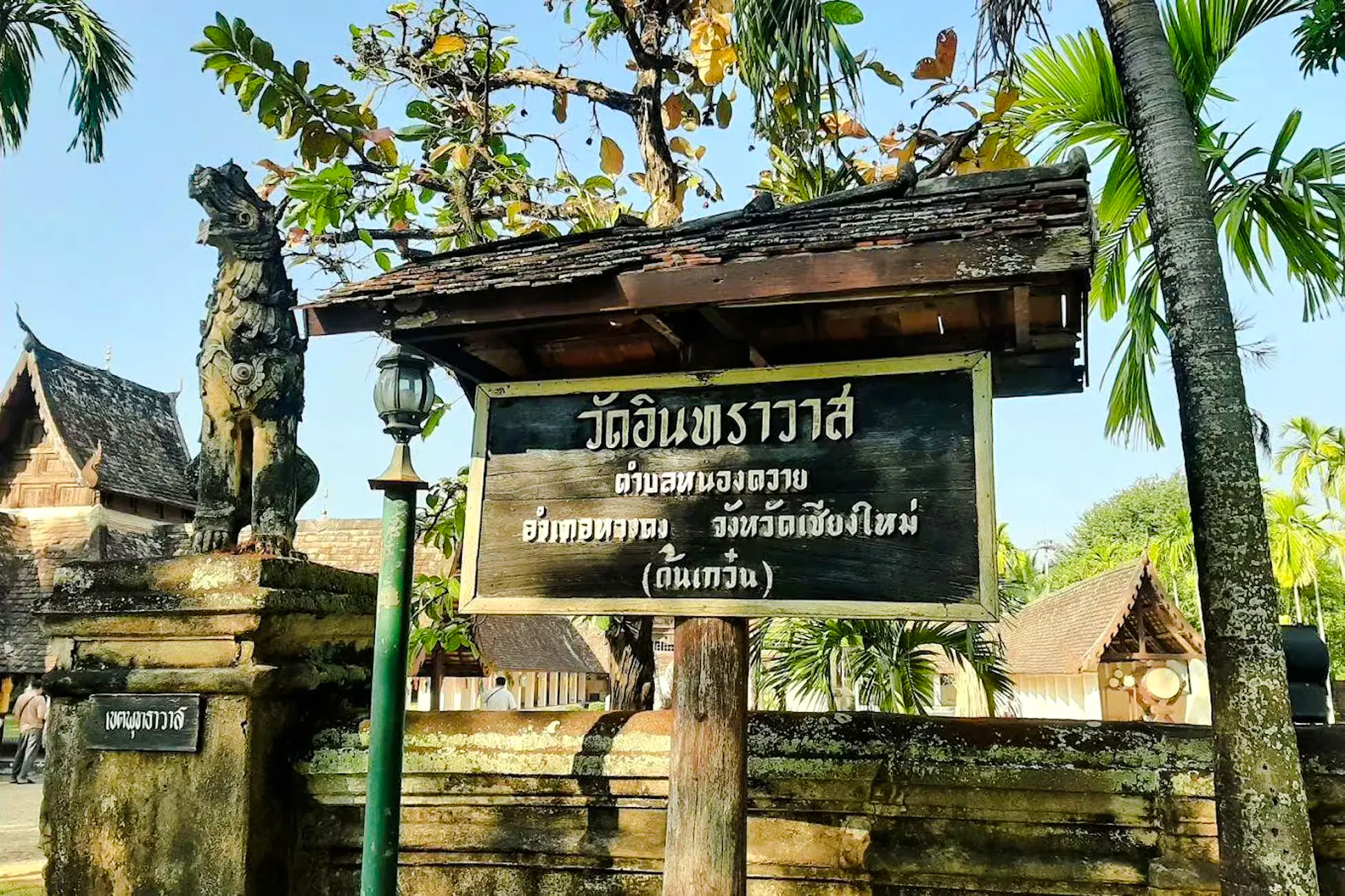 Chiang Mai temple entrance sign with traditional architecture and guardian statue.