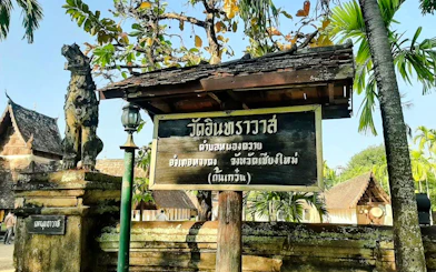 Chiang Mai temple entrance sign with traditional architecture and guardian statue.