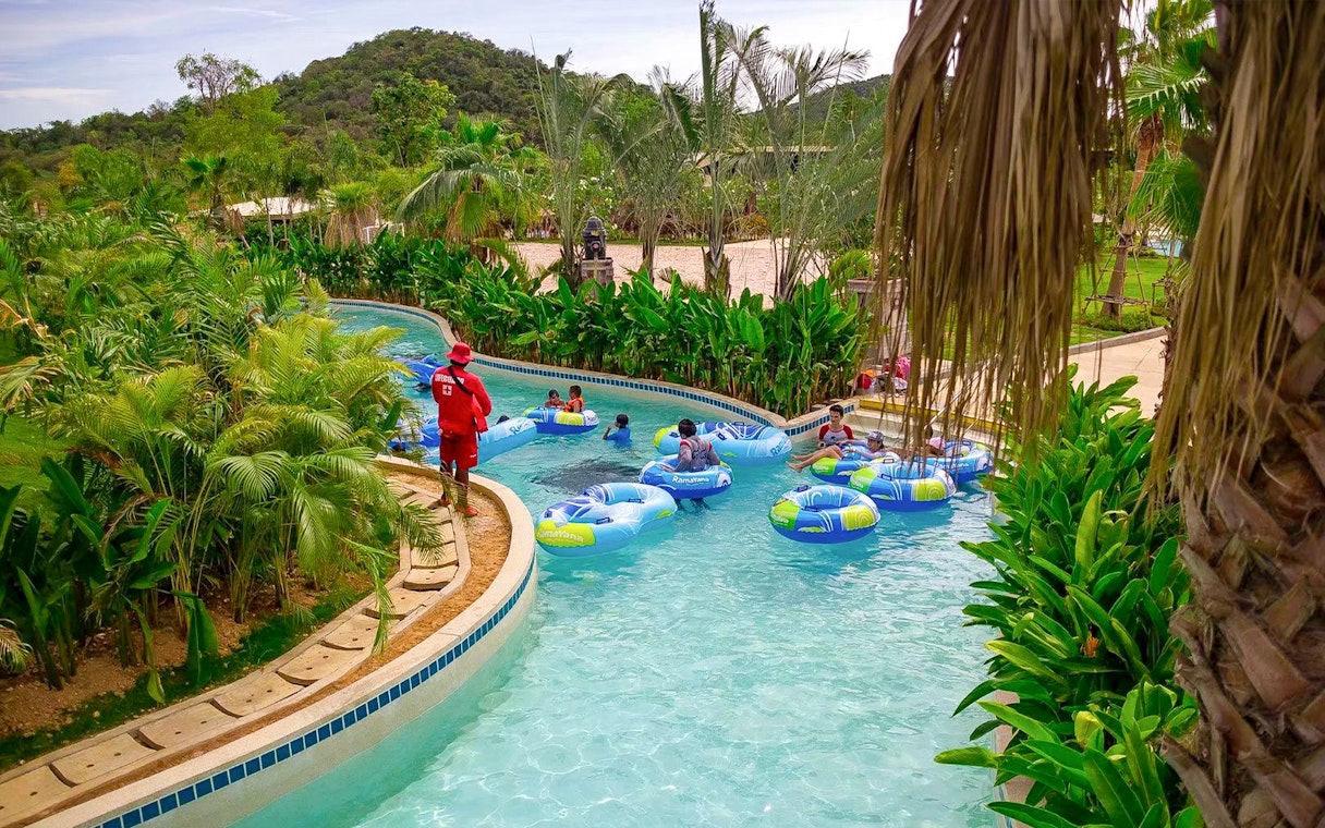 Visitors floating on inflatable tubes in a lazy river at Ramayana Water Park, surrounded by lush greenery.