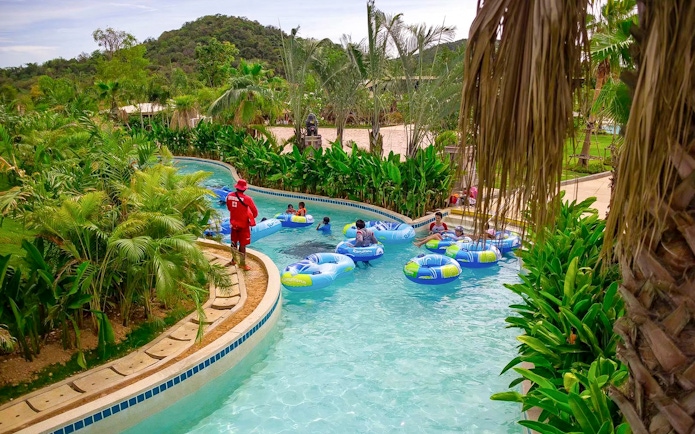 Visitors floating on inflatable tubes in a lazy river at Ramayana Water Park, surrounded by lush greenery.