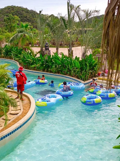 Visitors floating on inflatable tubes in a lazy river at Ramayana Water Park, surrounded by lush greenery.
