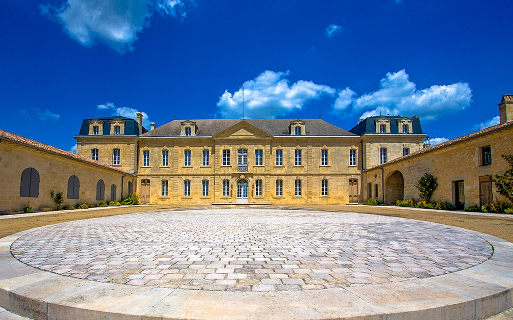 Saint Emilion winery courtyard with historic building under blue sky.