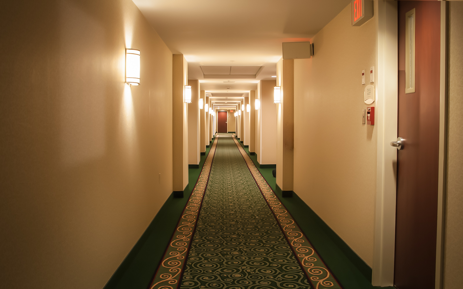 Empty hotel hallway with patterned carpet and wall lights.