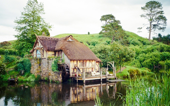 Mill house with water wheel on Hobbiton movie set tour, surrounded by lush greenery.