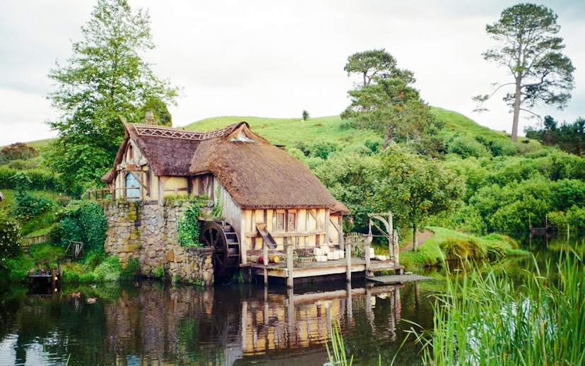 Mill house with water wheel on Hobbiton movie set tour, surrounded by lush greenery.