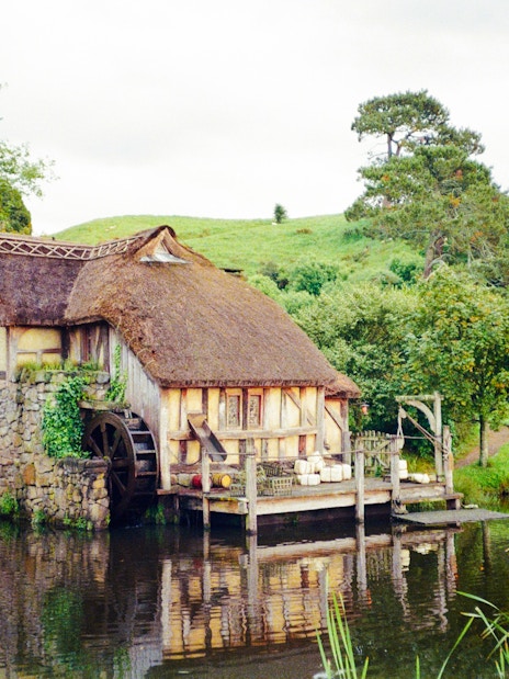 Mill house with water wheel on Hobbiton movie set tour, surrounded by lush greenery.