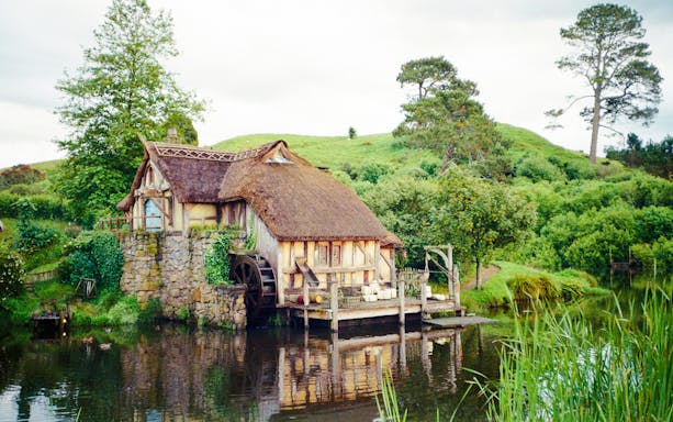 Mill house with water wheel on Hobbiton movie set tour, surrounded by lush greenery.