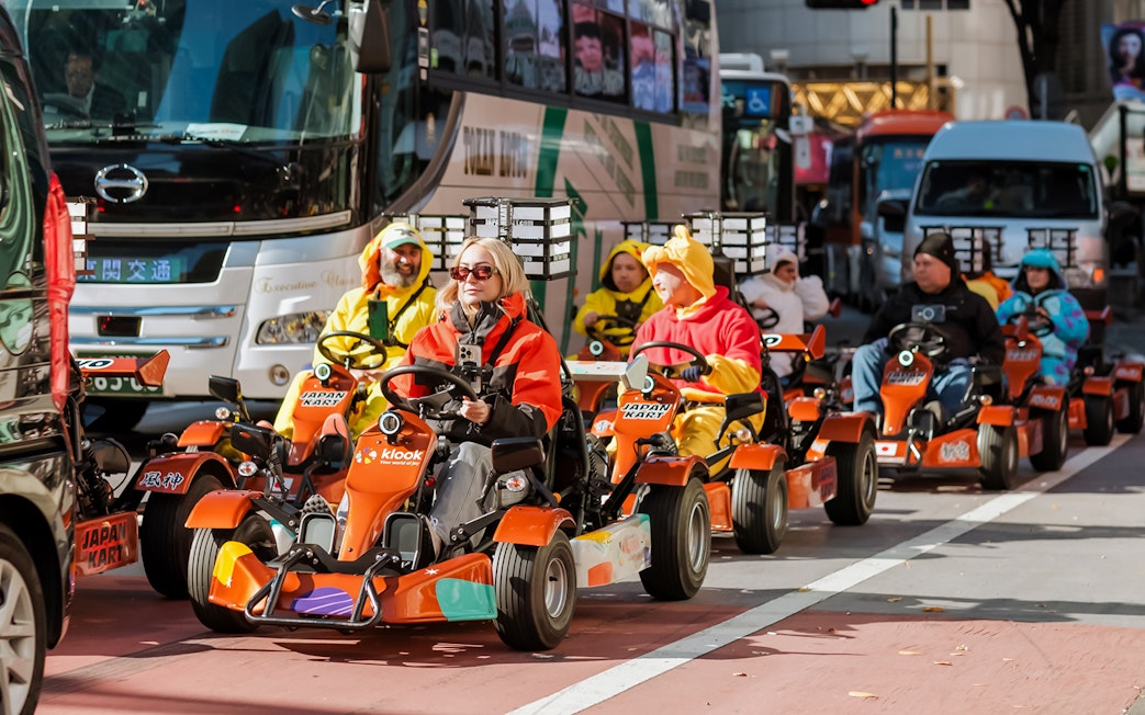 Tourists driving go-karts in Shibuya, Tokyo, dressed in colorful costumes.