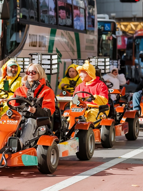 Tourists driving go-karts in Shibuya, Tokyo, dressed in colorful costumes.