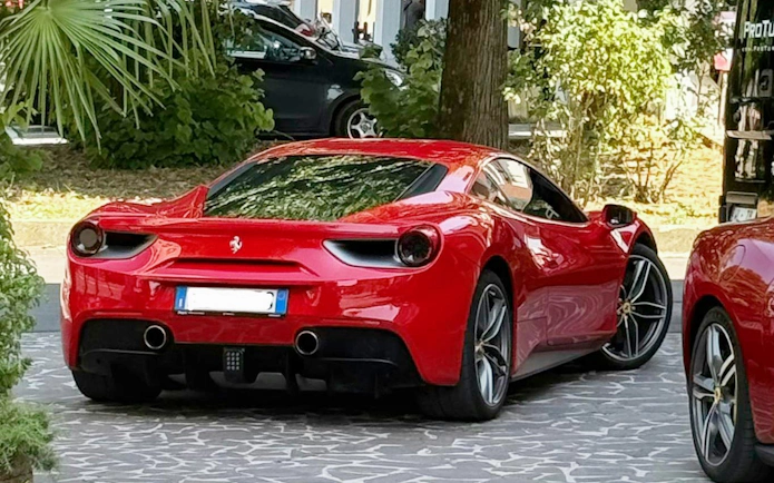 Red Ferrari 488 parked on a stone driveway surrounded by greenery.