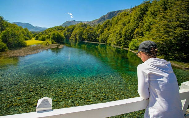 Visitor admiring the clear Manso River surrounded by lush Patagonian forest.