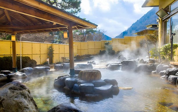 Outdoor hot spring at Hakone Kowakien Yunessun with steam rising from water.