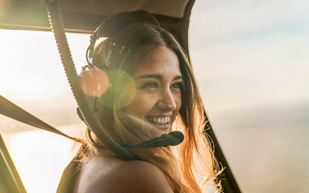 Visitor smiling inside a helicopter with headset, enjoying the aerial view.
