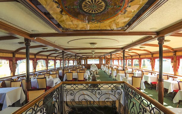 Elegant dining area on a Budapest evening dinner cruise ship with set tables and decorative ceiling.