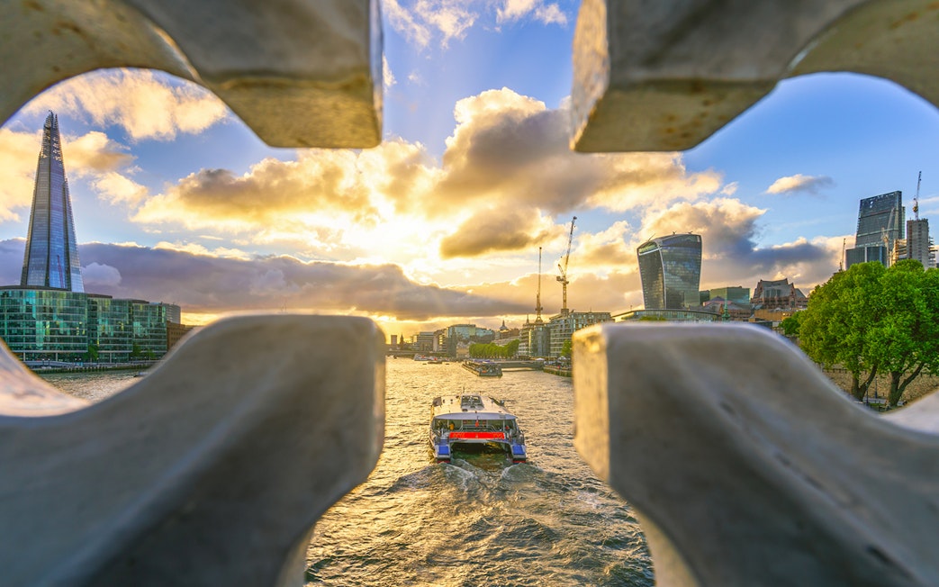 London skyline with Shard and Thames River cruise boat at sunset.