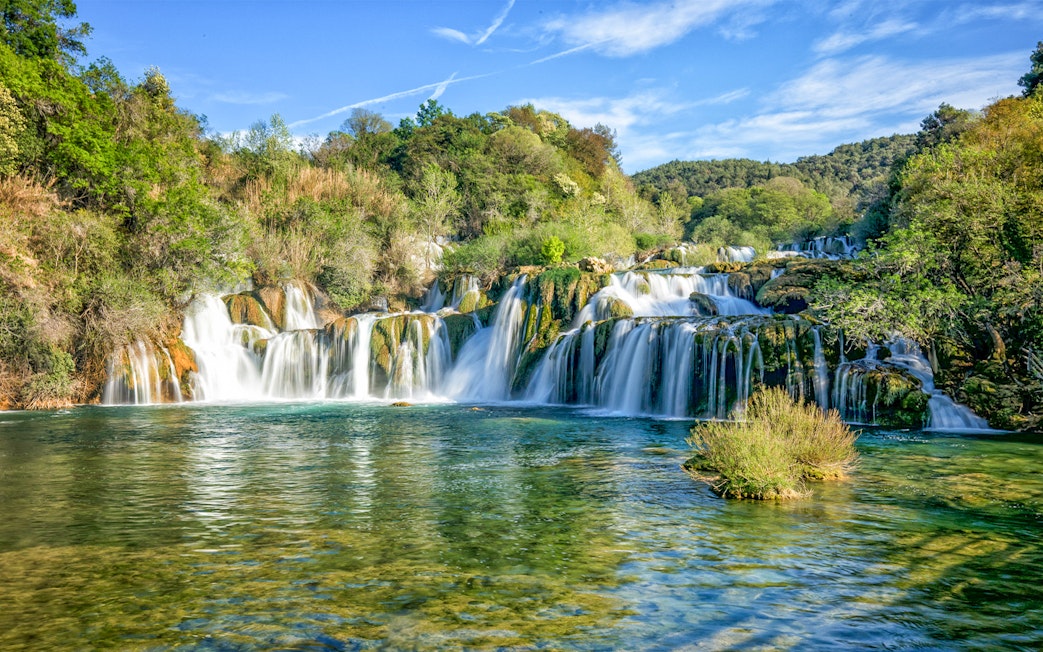 Waterfalls cascading over rocks at Krka National Park, surrounded by lush greenery.