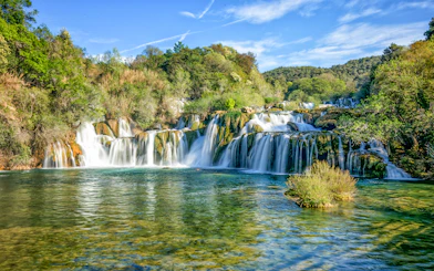 Waterfalls cascading over rocks at Krka National Park, surrounded by lush greenery.