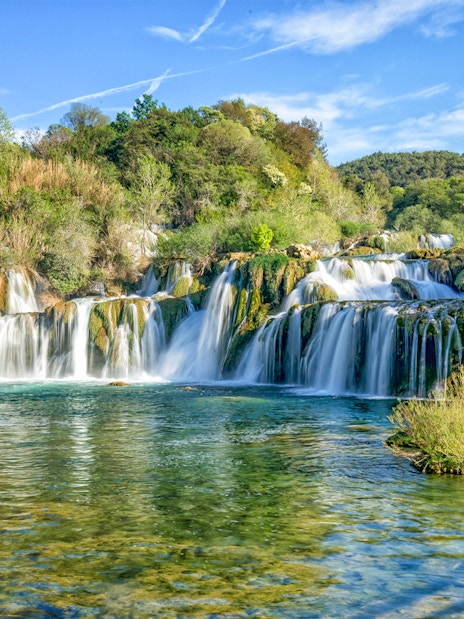 Waterfalls cascading over rocks at Krka National Park, surrounded by lush greenery.