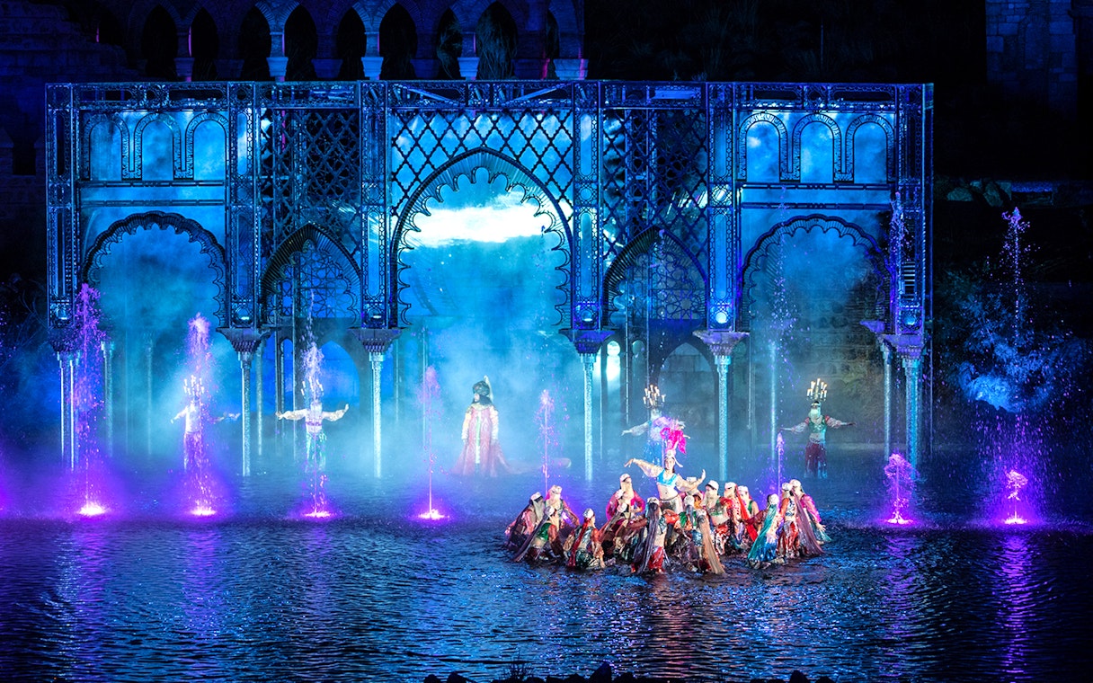 Performers in colorful costumes at The Dream of Toledo Night Show with illuminated arches and fountains.