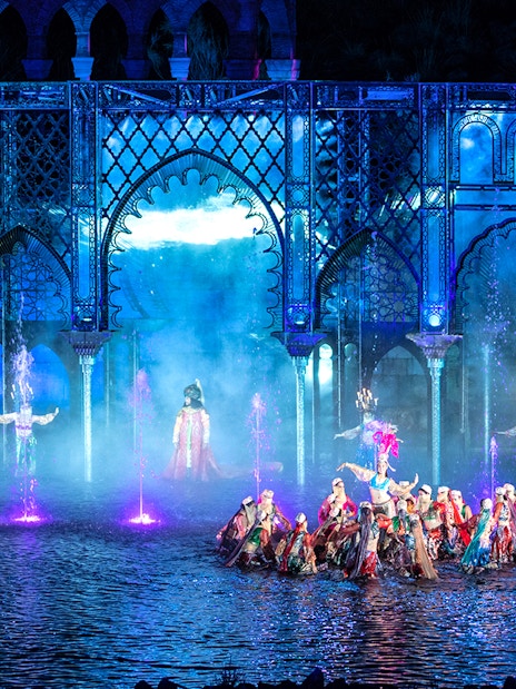 Performers in colorful costumes at The Dream of Toledo Night Show with illuminated arches and fountains.
