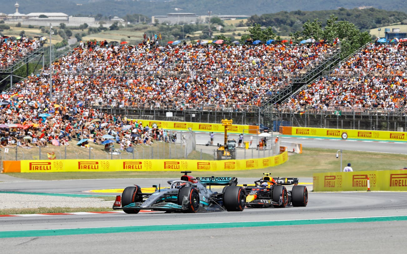 Formula 1 cars racing on track in Barcelona with a large crowd in the stands.