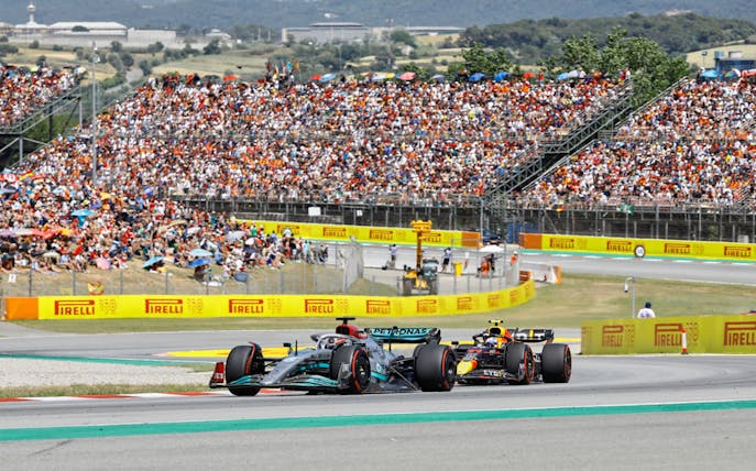 Formula 1 cars racing on track in Barcelona with a large crowd in the stands.