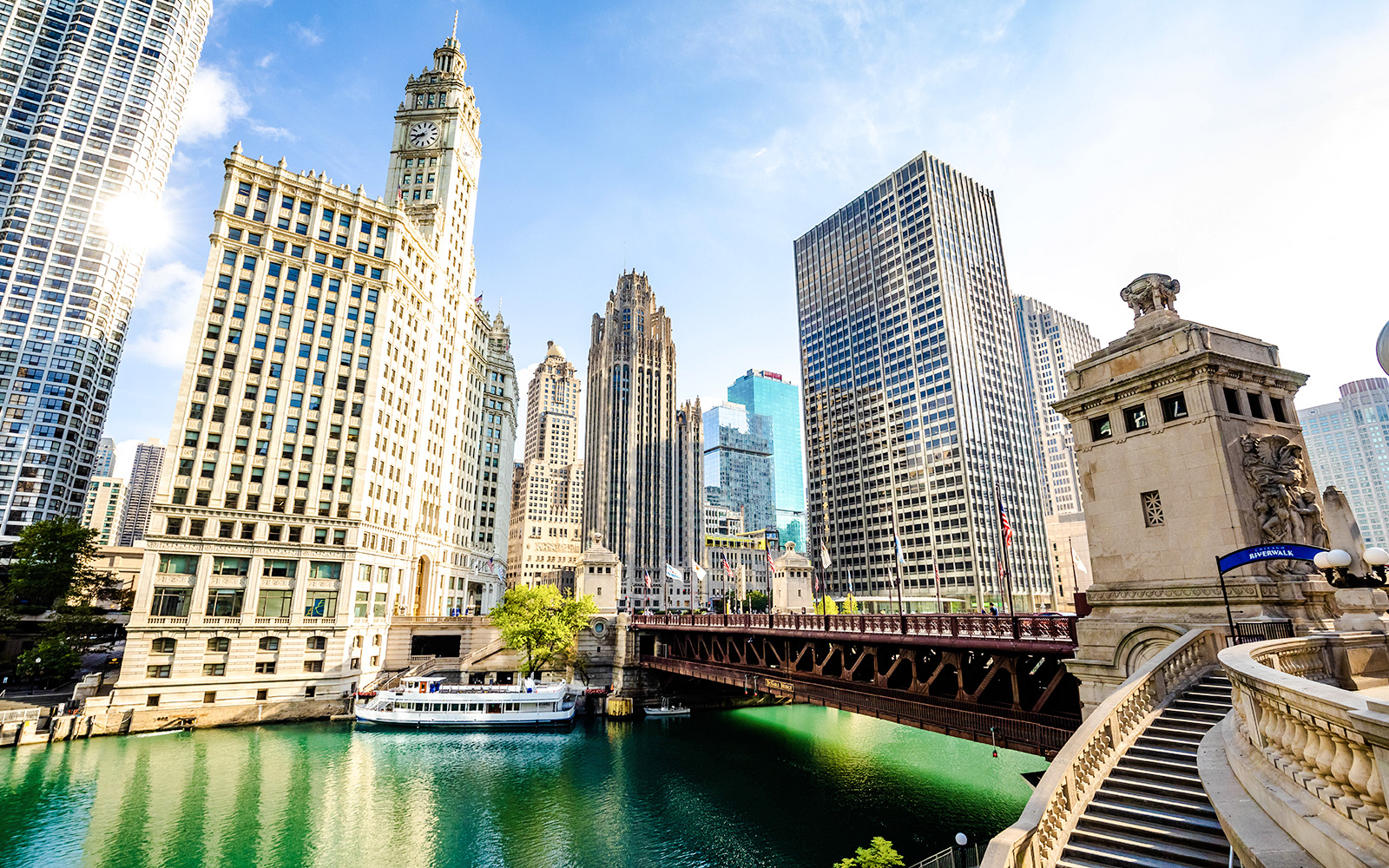 Chicago River with skyscrapers and a tour boat near the Wrigley Building and DuSable Bridge.