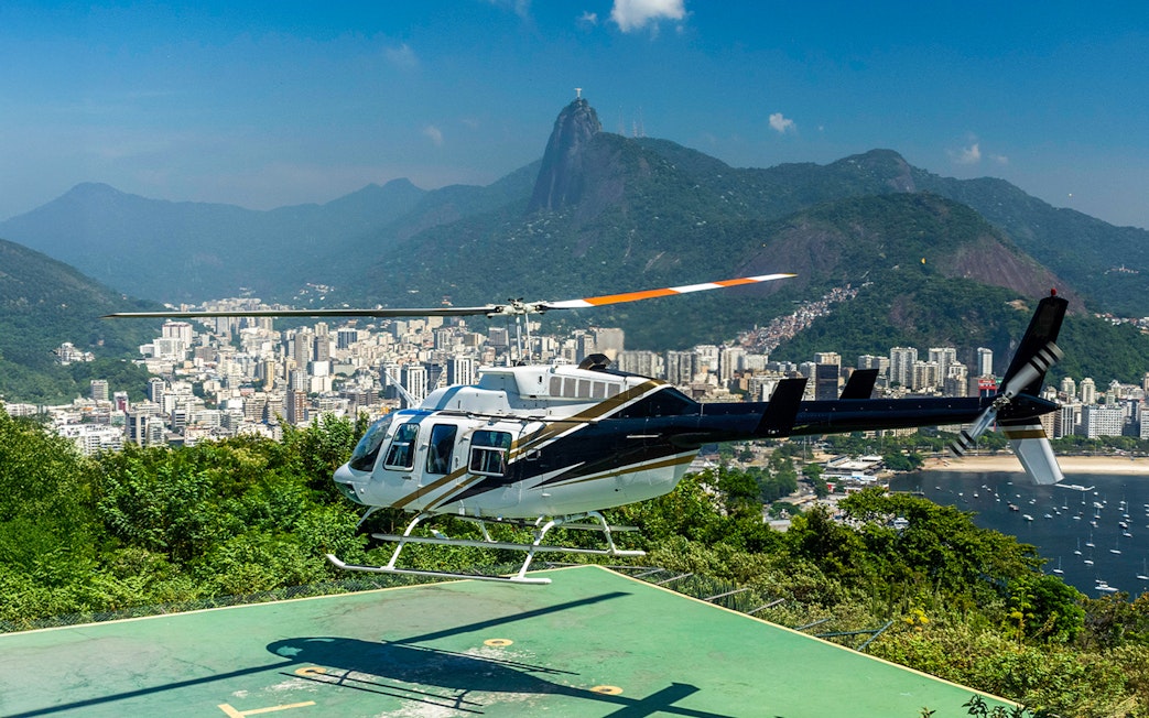 Helicopter taking off from Sugar Loaf Mountain with Rio de Janeiro cityscape in the background.