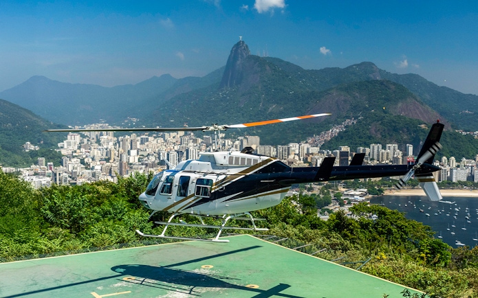Helicopter taking off from Sugar Loaf Mountain with Rio de Janeiro cityscape in the background.