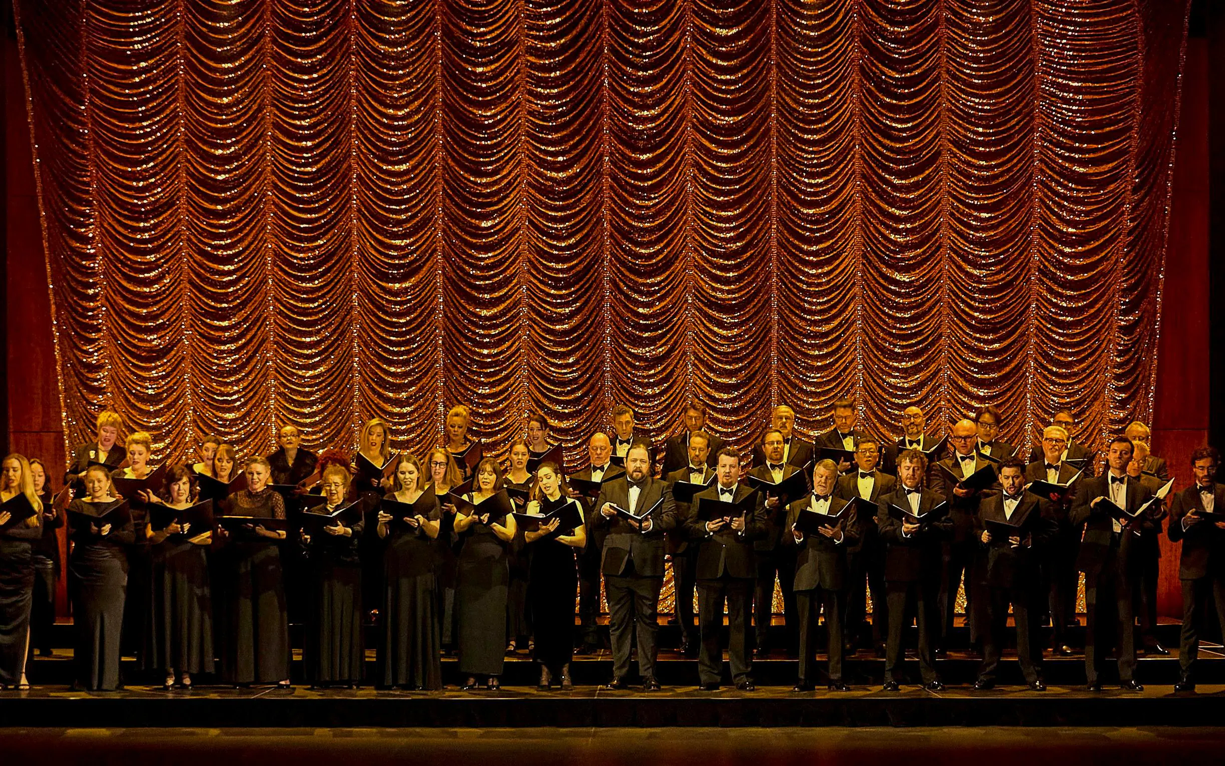 Chorus performing on stage with ornate curtain backdrop during My Fair Lady show.