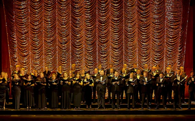 Chorus performing on stage with ornate curtain backdrop during My Fair Lady show.