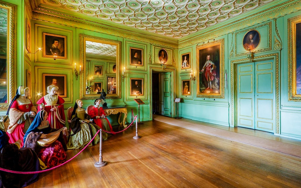 Warwick Castle interior with historical figures and portraits on green walls.
