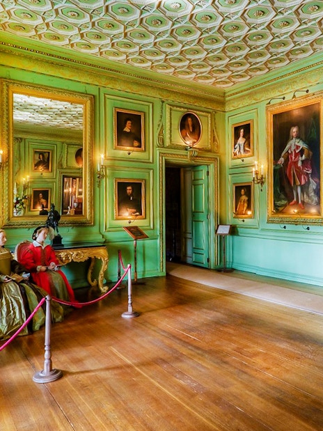 Warwick Castle interior with historical figures and portraits on green walls.