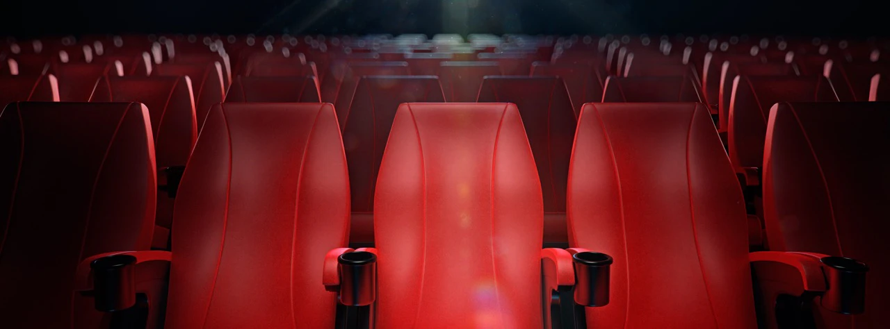 Rows of empty red theater seats under dim lighting.