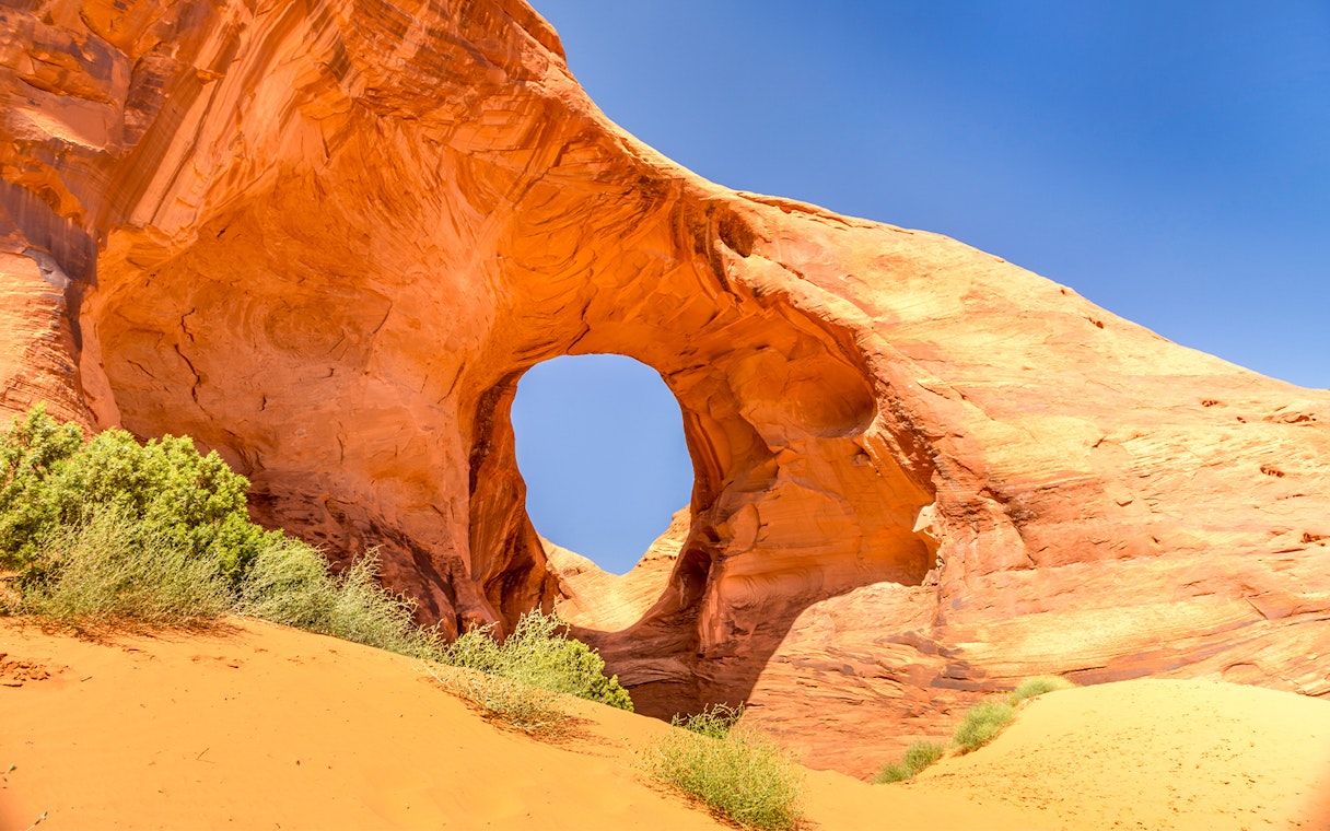 Ear of the Wind Arch in Monument Valley with clear blue sky.
