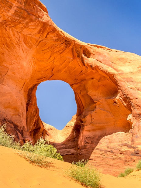Ear of the Wind Arch in Monument Valley with clear blue sky.