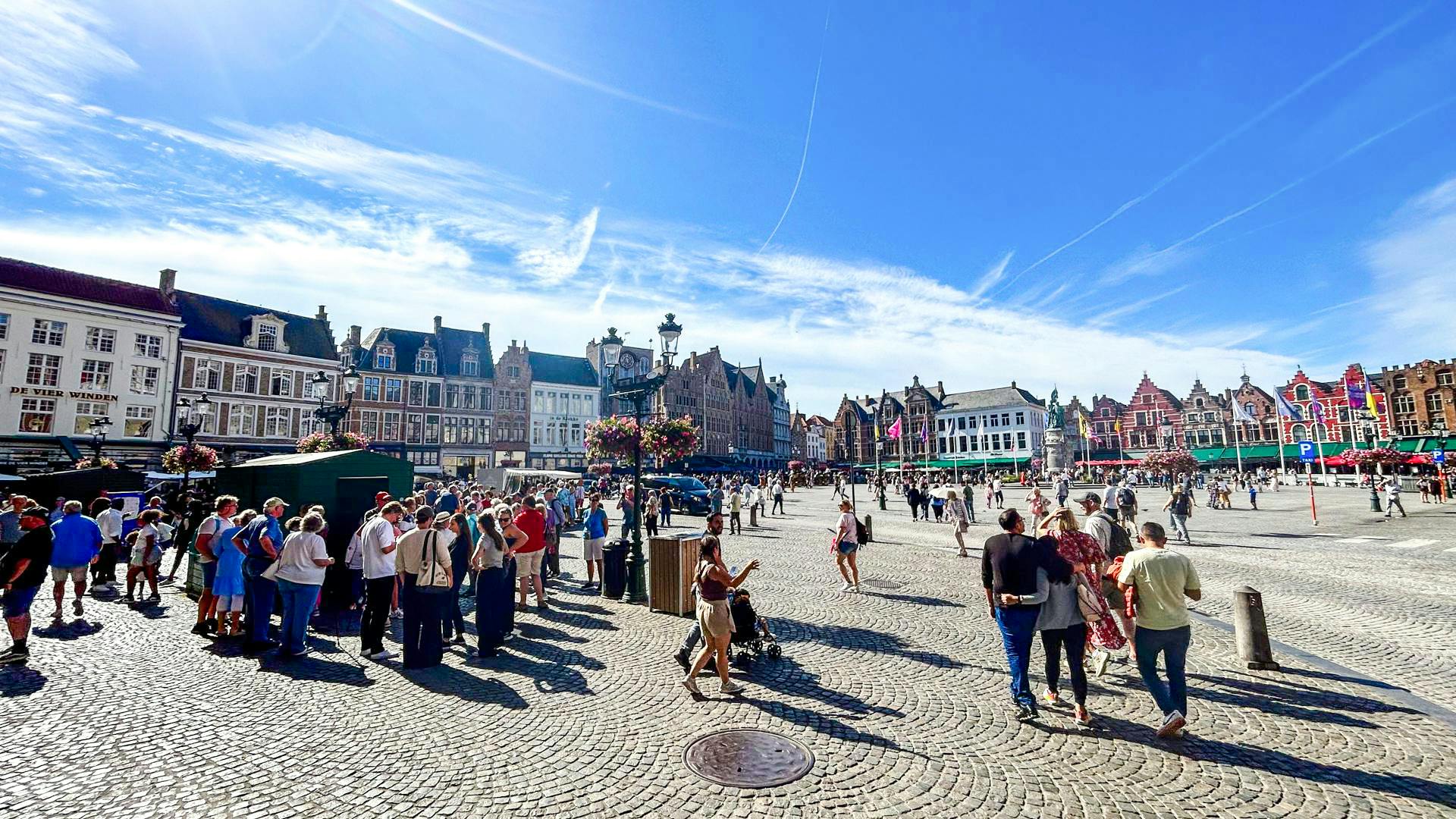 Crowd exploring Markt square with historic buildings in Bruges, Belgium.