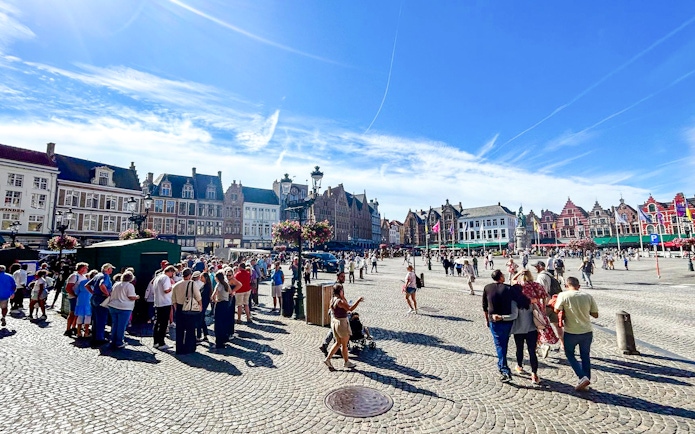 Crowd exploring Markt square with historic buildings in Bruges, Belgium.