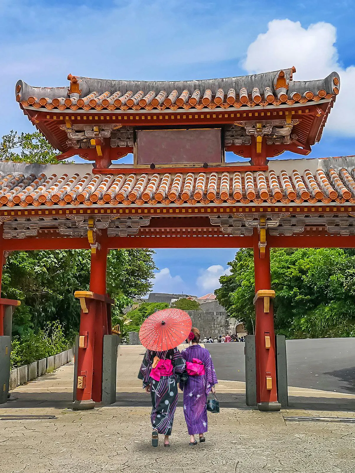 Visitors in traditional attire walk under Shureimon Gate, Okinawa.