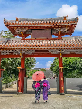 Visitors in traditional attire walk under Shureimon Gate, Okinawa.