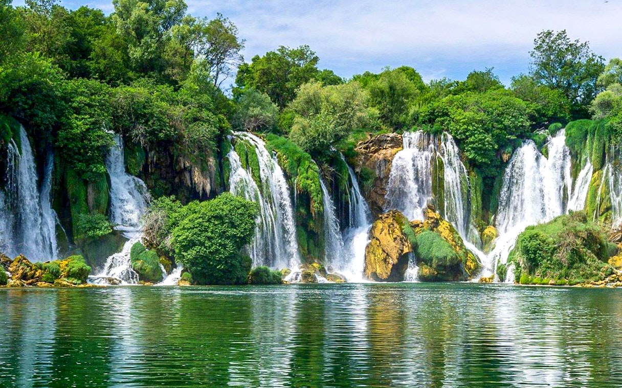 Kravica Waterfall cascading into a serene pool surrounded by lush greenery during a private tour.