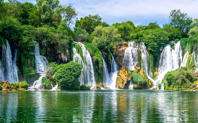 Kravica Waterfall cascading into a serene pool surrounded by lush greenery during a private tour.