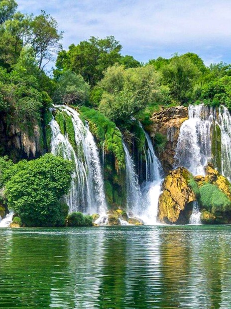 Kravica Waterfall cascading into a serene pool surrounded by lush greenery during a private tour.