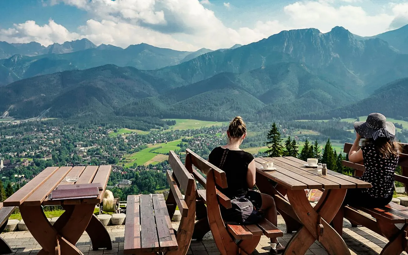 Benches overlooking Tatra Mountains in Zakopane, Poland, with visitors enjoying the view.
